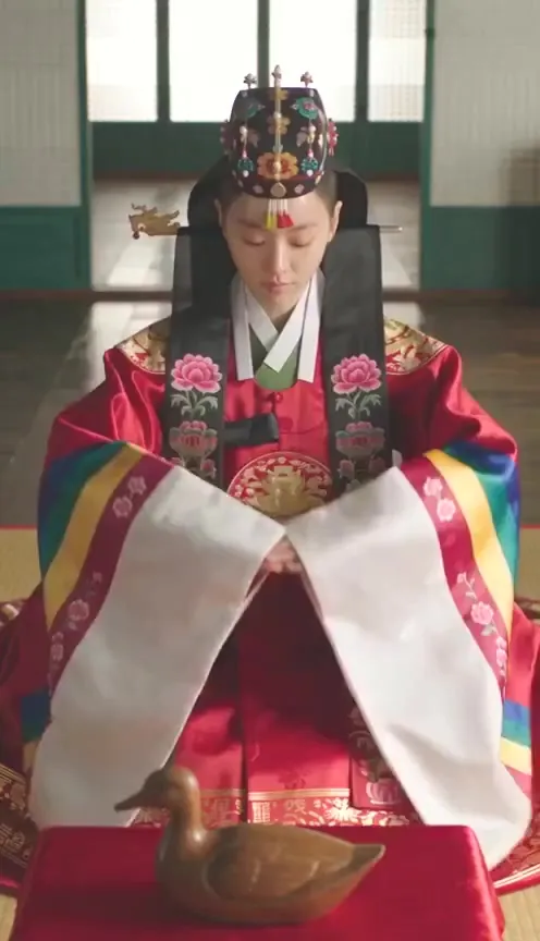 A bride in a red wedding robe bows before a wooden goose
