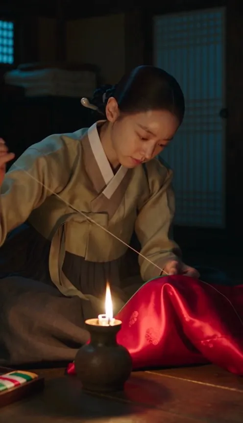 She sews by the light of a single oil lamp